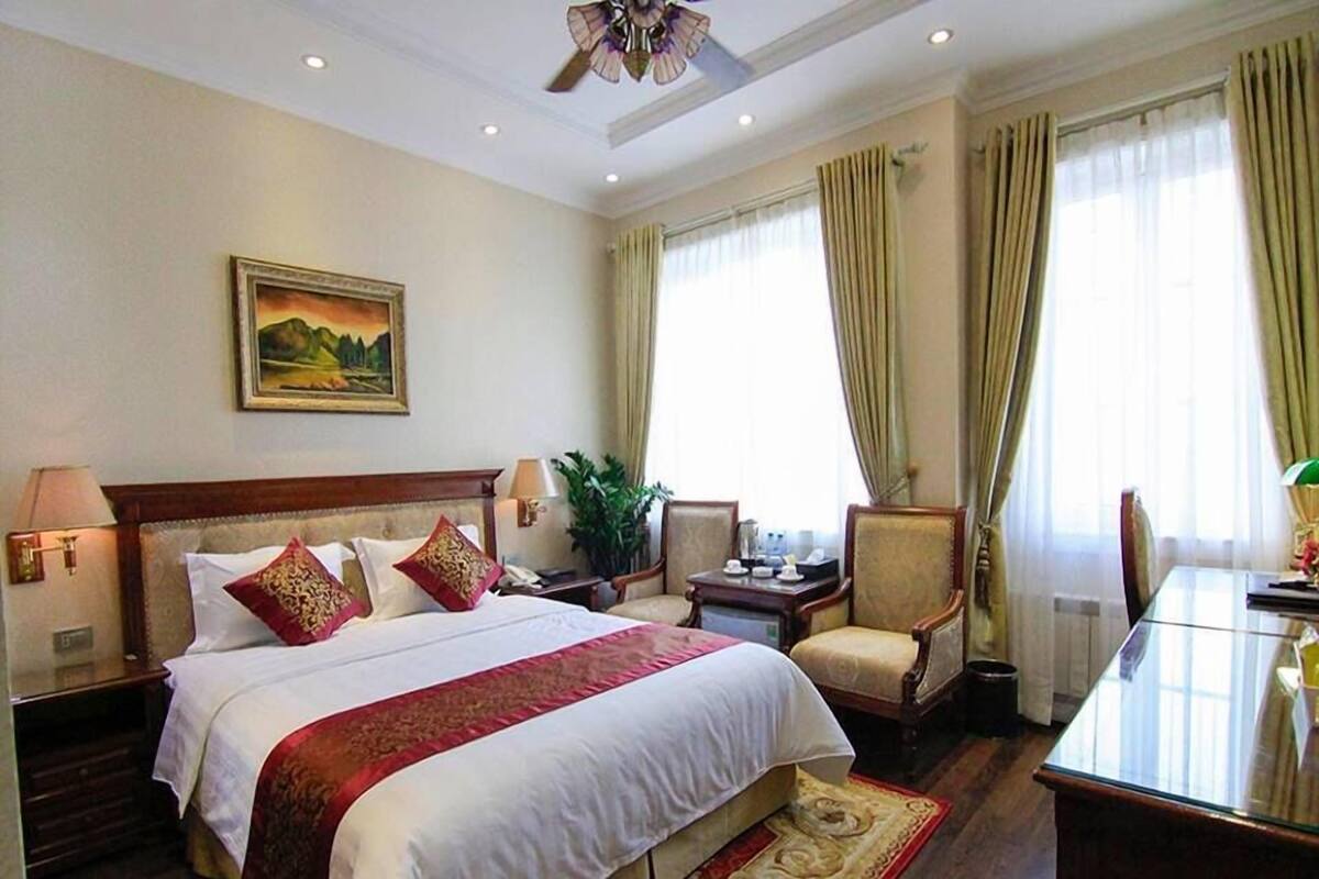 Habitación de hotel con una cama grande, un escritorio, una silla, una mesa y un cuadro en la pared.