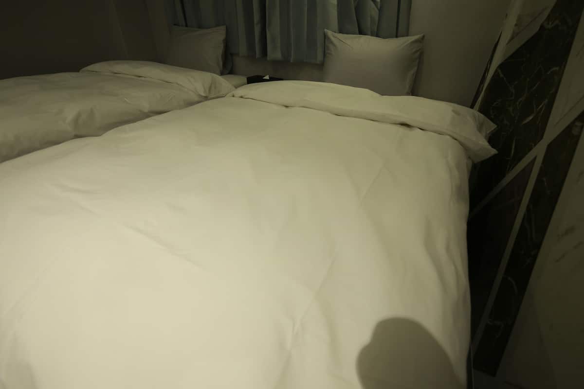 A bed with white bedding in a room with a curtain and a wall with a patterned design.