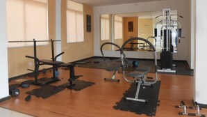 Et fitnessrum med træningsudstyr, store vinduer og en loftsvifte.