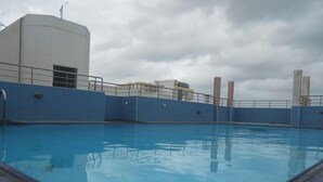 En swimmingpool med blå fliseterrasse og en hvid bygning i baggrunden.