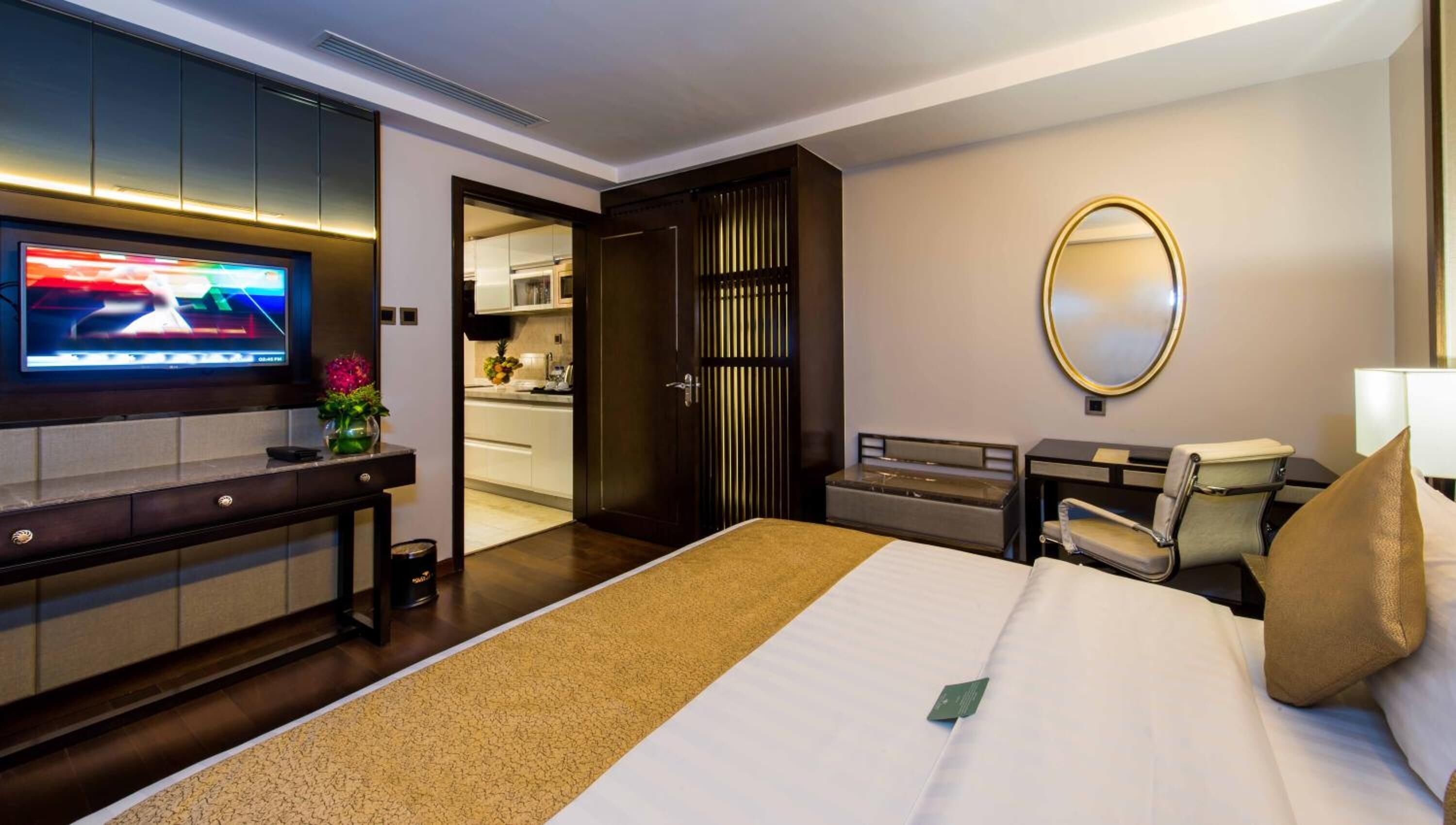 A hotel room with a bed, a TV, a desk, a chair, a mirror, and a door leading to a bathroom.