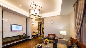 A modern living room with a flat-screen TV, a coffee table with a vase of flowers, a sofa with patterned cushions, and a dining area in the background. - Boudl Gaber (Riyadh)