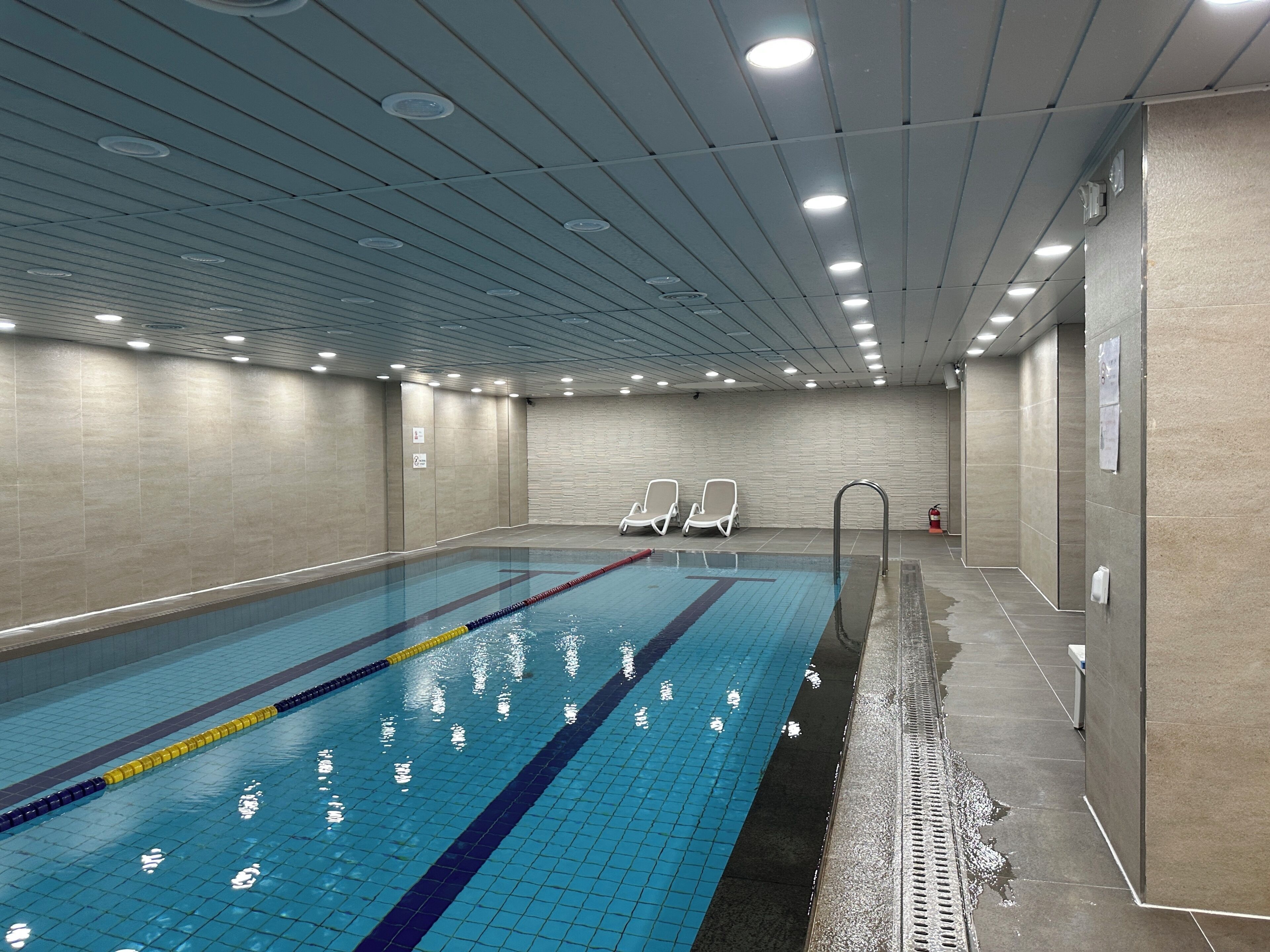 Une piscine intérieure dotée de couloirs clairement délimités, d’un mur carrelé et d’un plafond avec des spots encastrés.