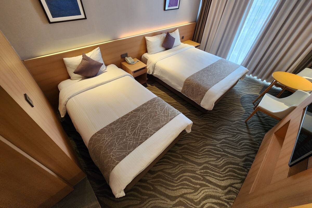 A hotel room with two beds, a small desk, and a chair.