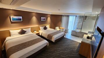 A hotel room with two beds, a desk, a chair, a small table, a mirror, and a bathroom with a glass shower.