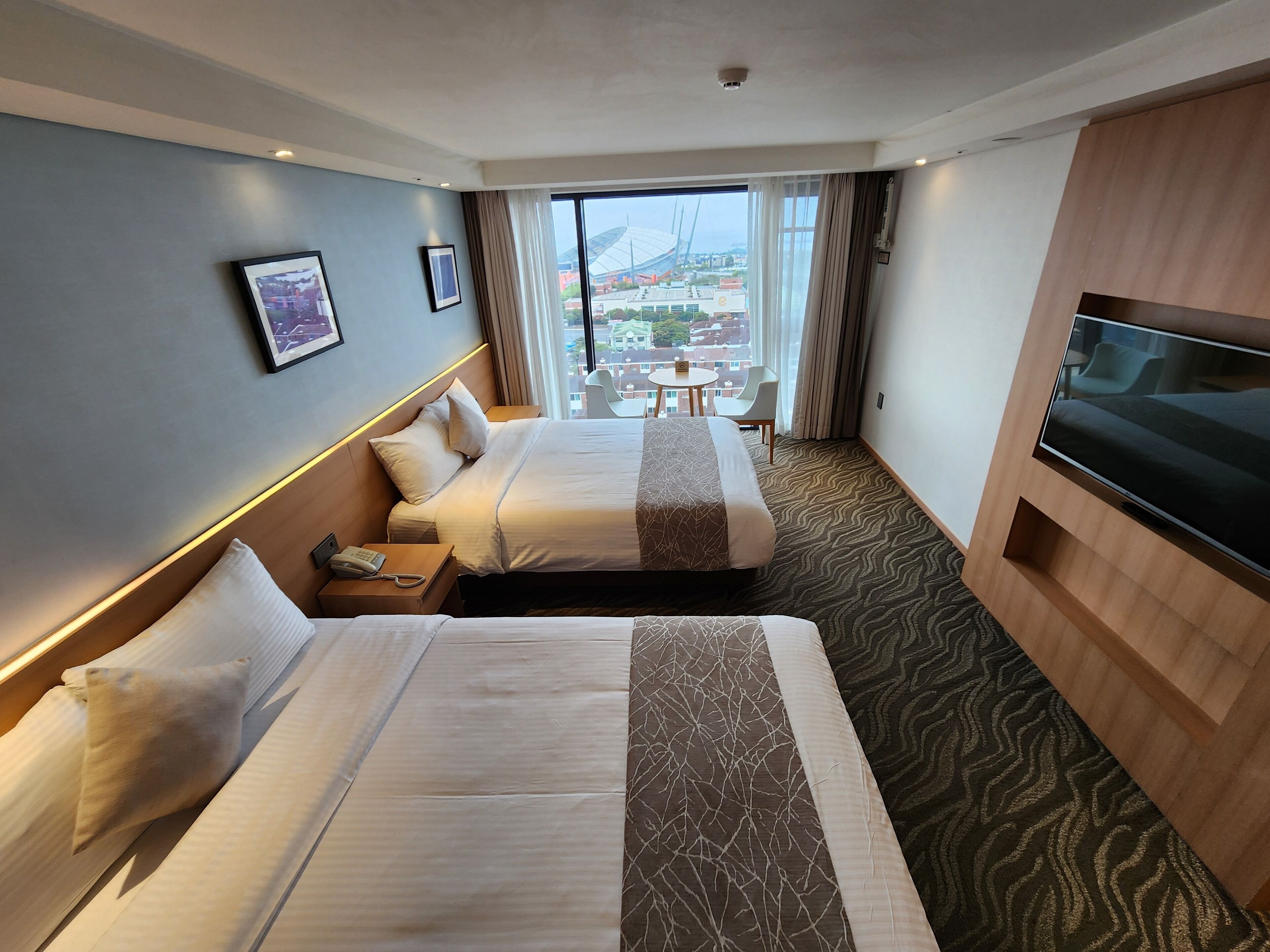 Une chambre d’hôtel avec deux lits, une télévision, une petite table et une vue sur la ville.