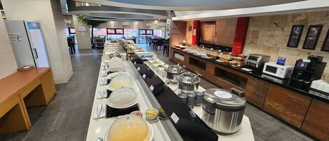 A buffet setup with various food stations, a coffee machine, and a microwave.