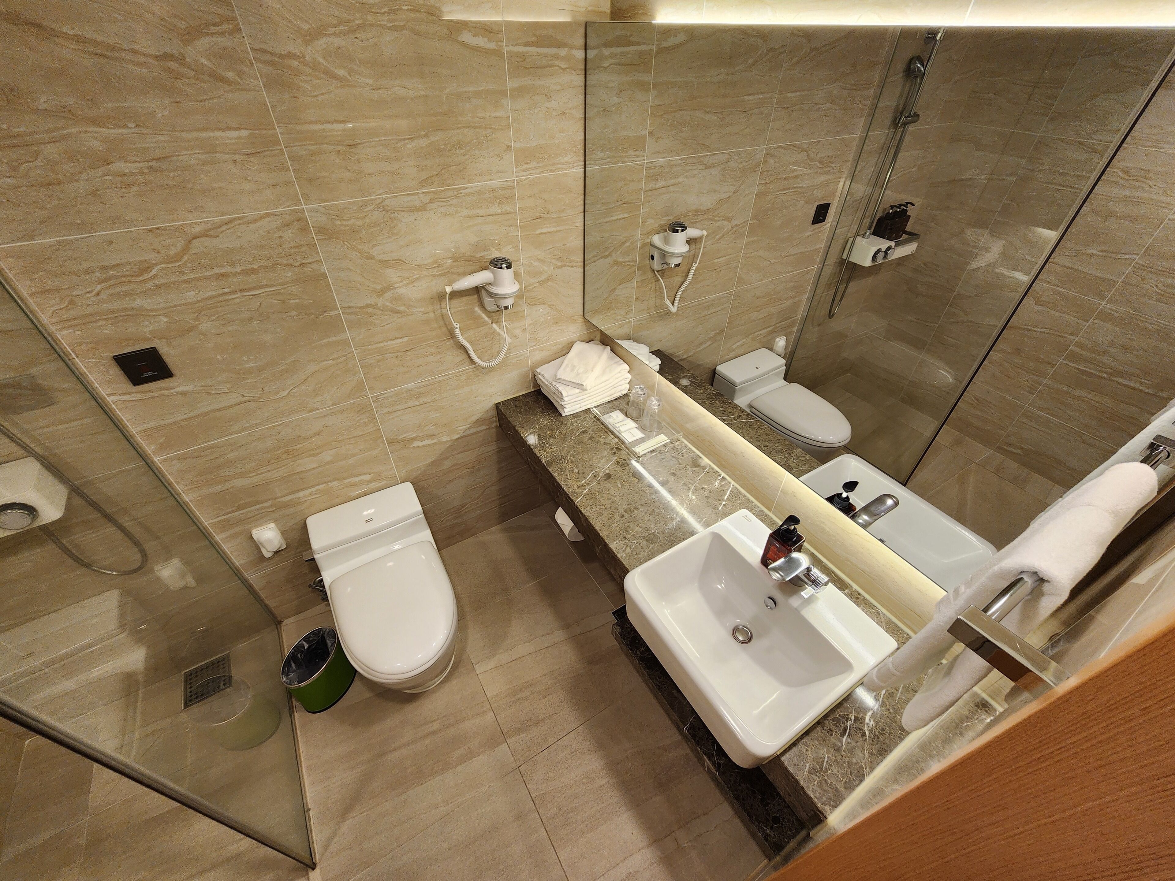 A modern bathroom with a marble floor, a glass-enclosed shower, a toilet, a sink with a mirror, and a towel rack.