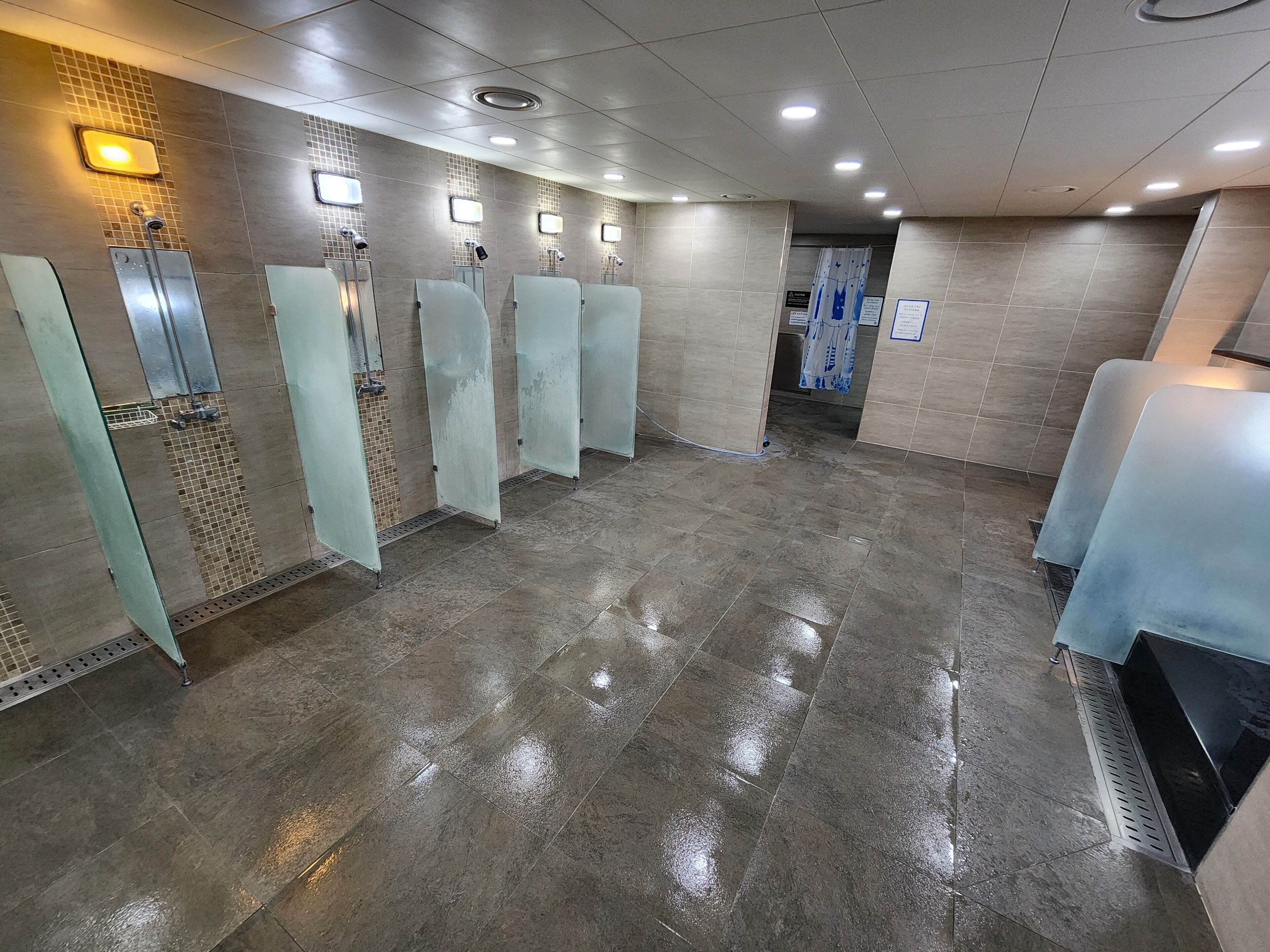 A public restroom with multiple urinals, a tiled floor, and overhead lighting.