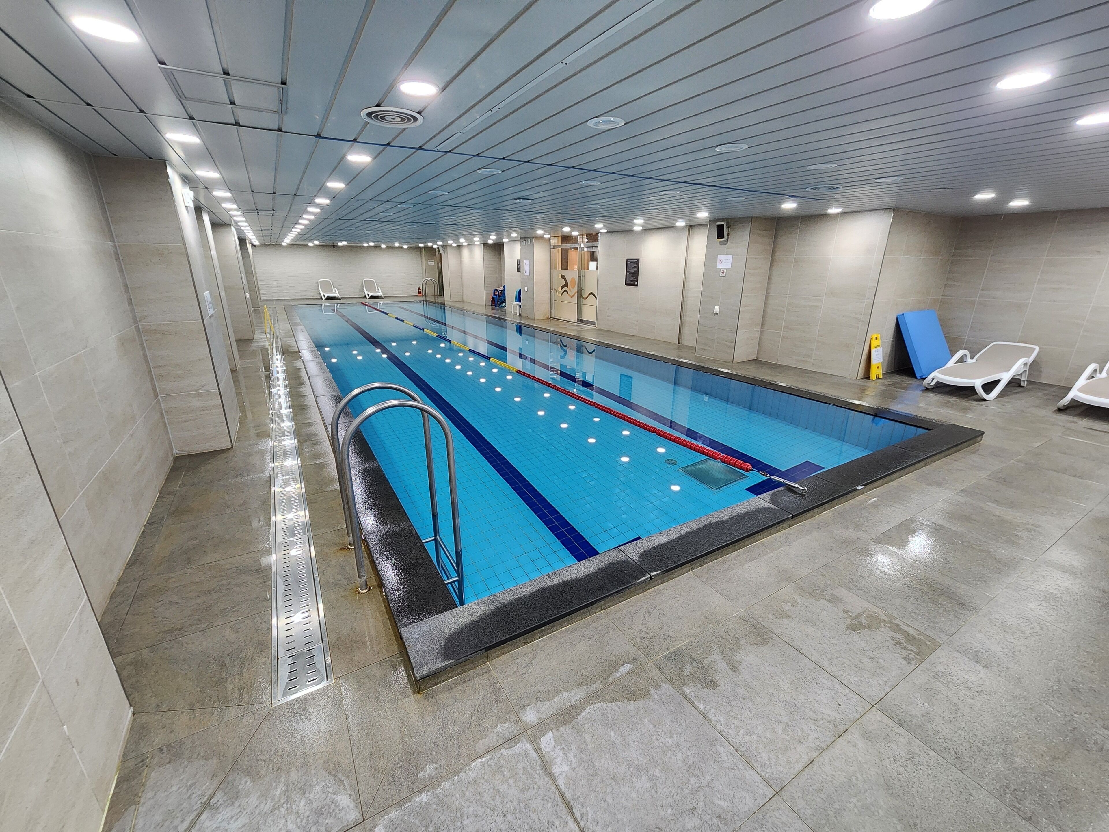 An indoor swimming pool with clear lanes, a metal ladder, and tiled walls.