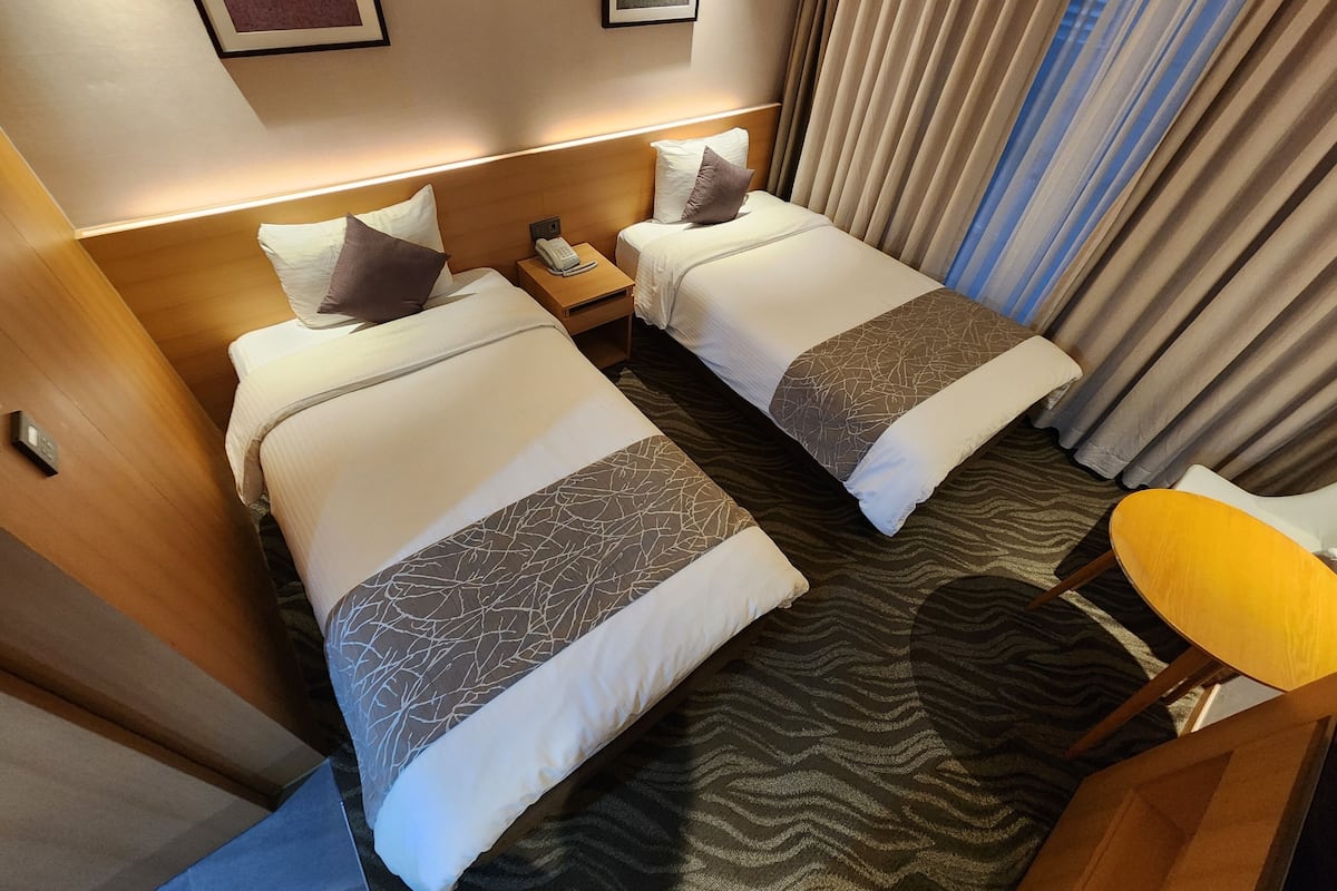 A hotel room with two beds, a bedside table with a phone, and a small table with a chair.