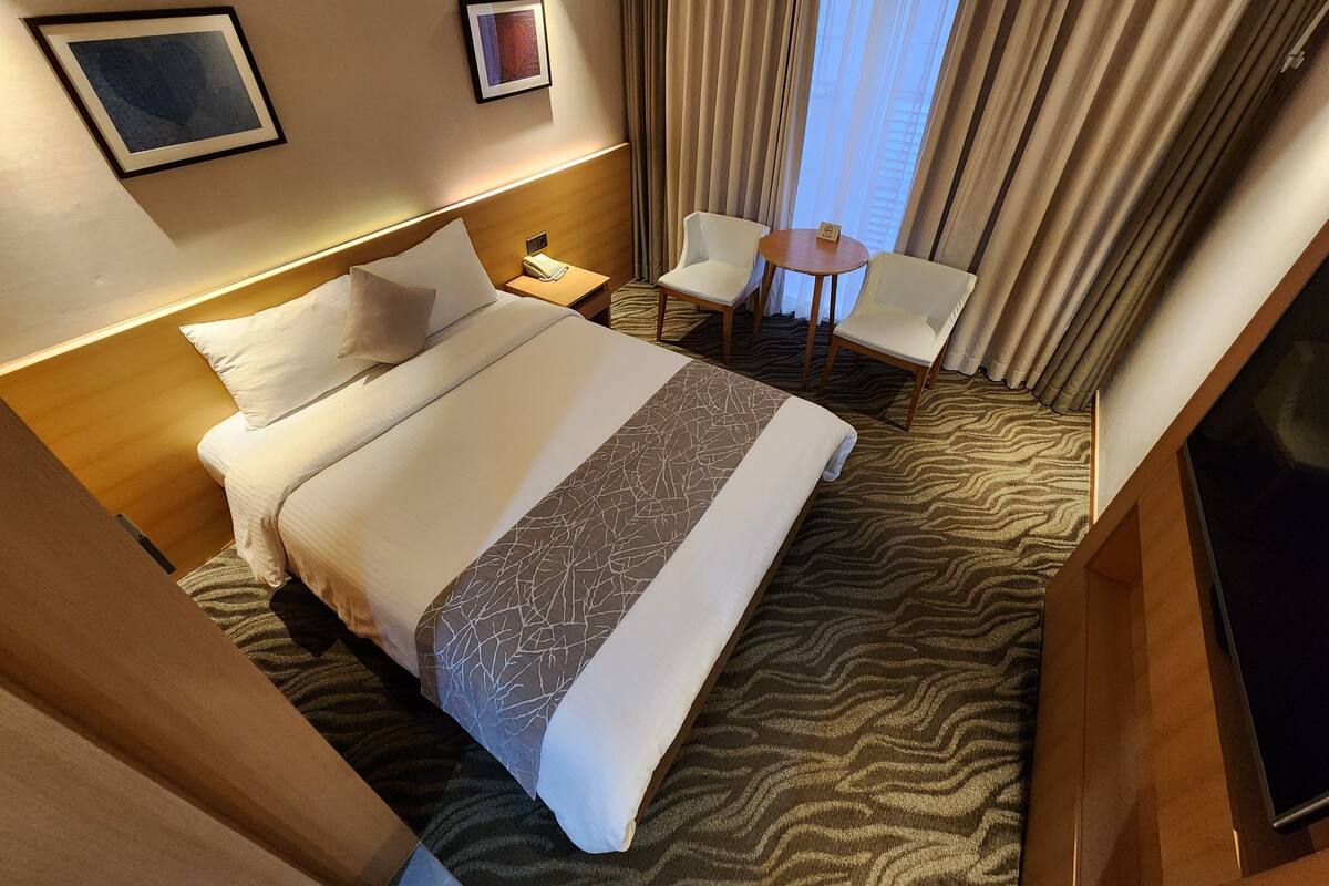 A hotel room with a large bed, a bedside table, a chair, a small table, and a TV.