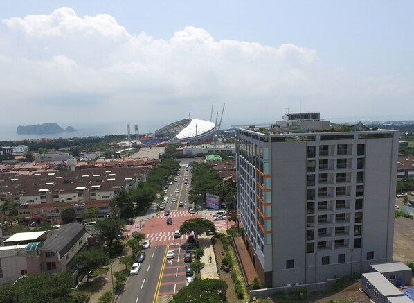 Um edifício alto com design moderno, rodeado por um horizonte urbano com um estádio e uma ponte ao fundo.
