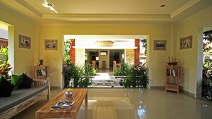 A spacious lobby with a polished floor, a wooden coffee table, a sofa with cushions, and a bookshelf. - Uma de Villa Sanur (Denpasar)