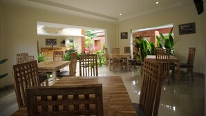 A spacious dining area with wooden furniture and a view of a garden through an open archway. - Uma de Villa Sanur (Denpasar)