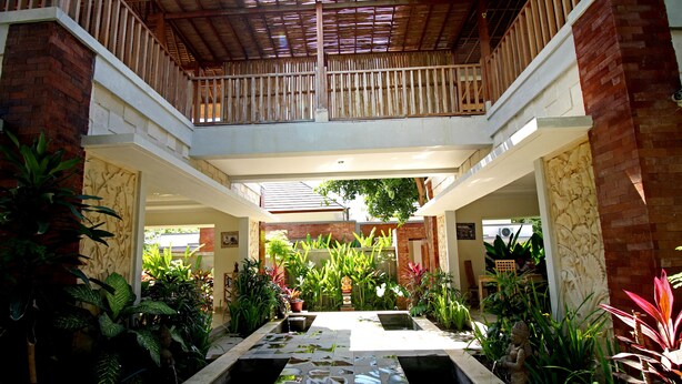 A spacious atrium with a central water feature, surrounded by lush greenery and a wooden balcony. - Uma de Villa Sanur (Denpasar)