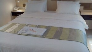 Un lit bien fait, avec des draps blancs, une couverture à rayures et une serviette pliée posée sur le lit.