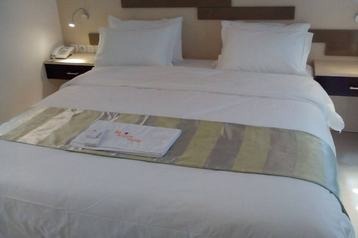 Ein ordentlich gemachtes Bett mit weißen Laken, einer gestreiften Decke und einem gefalteten Handtuch.