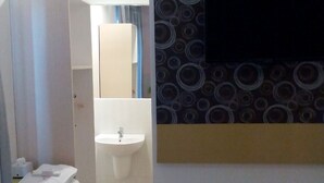 Une salle de bain d’hôtel équipée d’un lavabo, d’un miroir et d’un téléviseur fixé au mur.