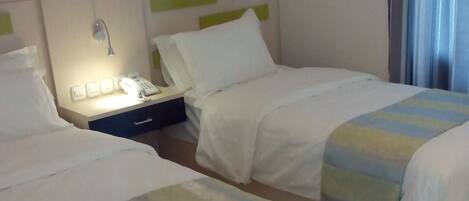 A hotel room with two beds, a bedside table with a phone, and a window with curtains.
