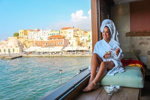 A person sitting by a window overlooking a waterfront with buildings in the background. - Vranas Residenza Signature Suites (Chania)