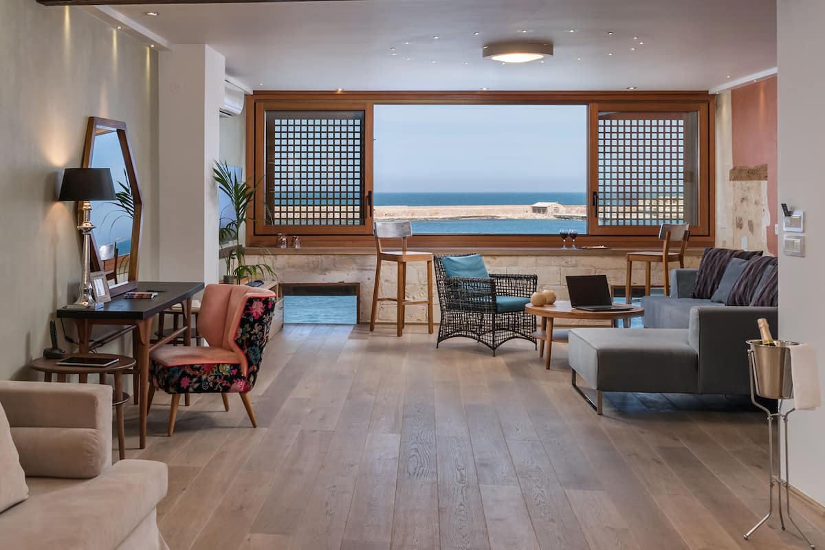 A spacious living room with a view of the sea, furnished with a sofa, chairs, and a table.