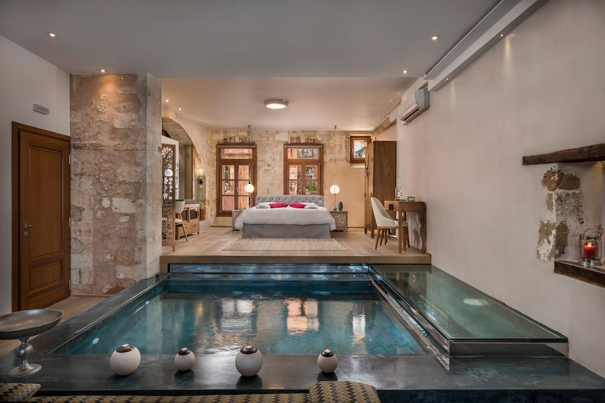 A bedroom with a large bed, a glass-enclosed pool, and a view of the room.