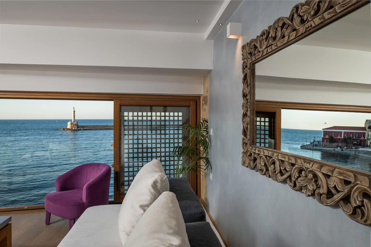A balcony with a view of the sea and a lighthouse, a purple armchair, and a large ornate mirror.
