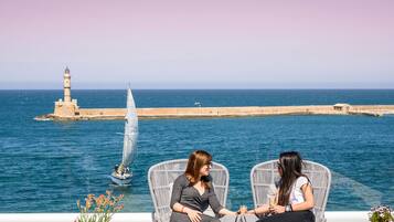 Two people seated on wicker chairs overlooking a body of water with a lighthouse in the background.