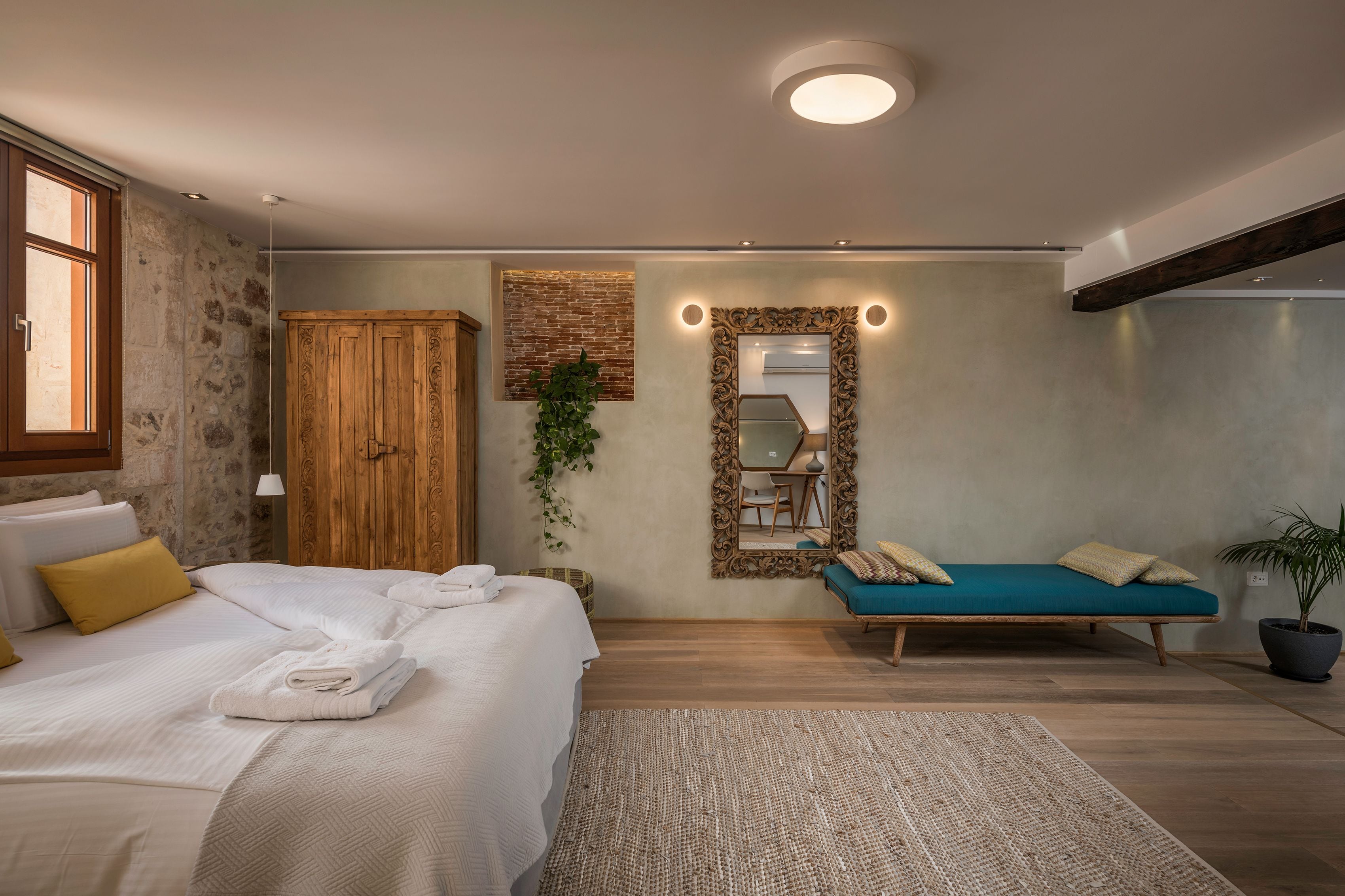 A bedroom with a bed, a sofa, a mirror, and a plant.