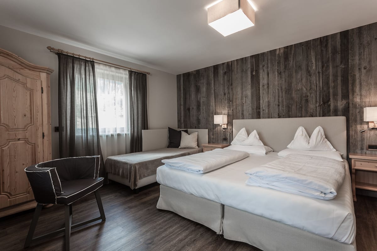Una habitación de hotel con dos camas, un armario de madera, una silla y un ventanal con cortinas.