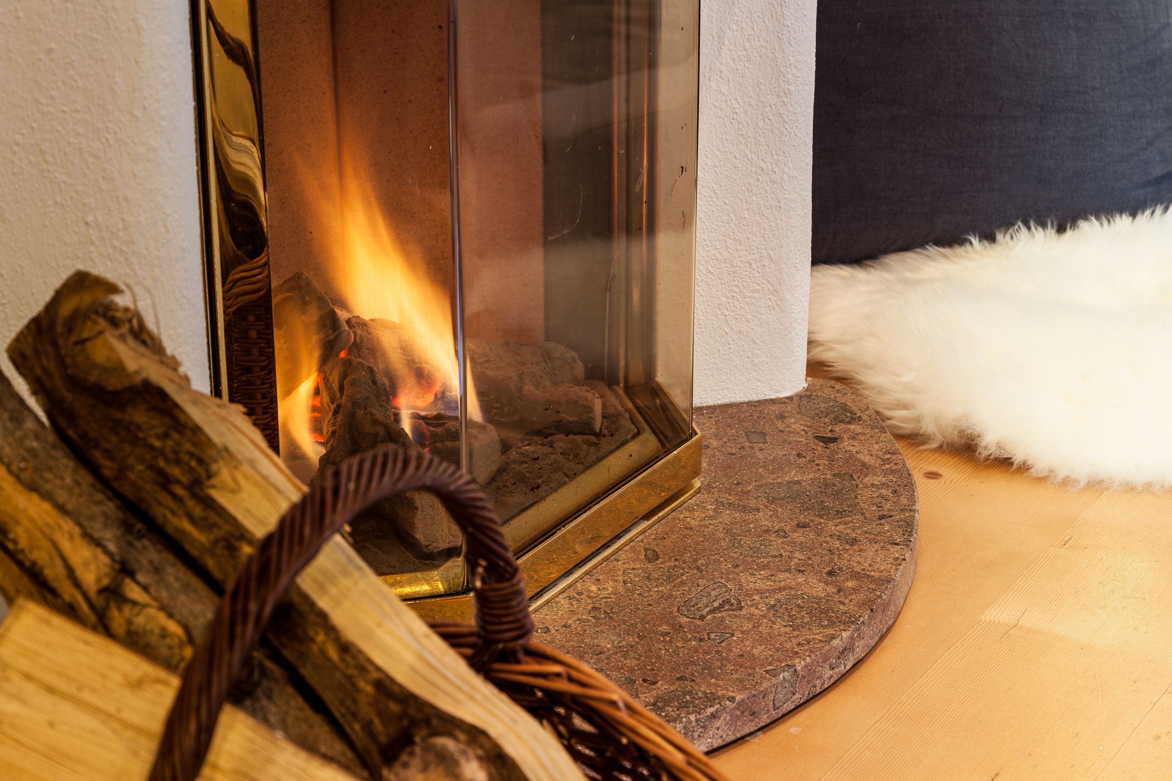 A fireplace with burning logs, a woven rug, and a white fluffy object on the floor.