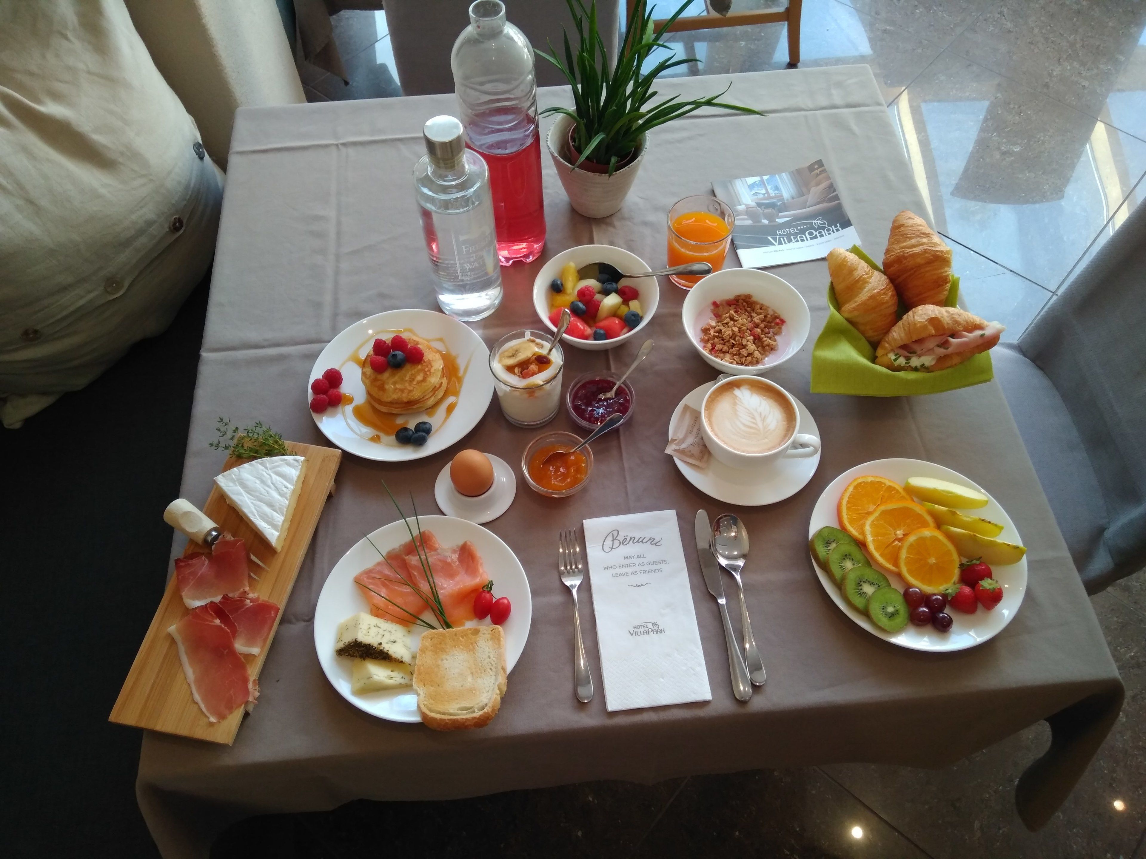 Une table de petit-déjeuner avec divers aliments, notamment des crêpes, des croissants et des fruits.