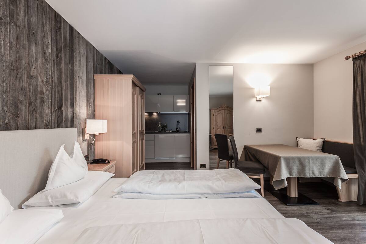 Una habitación de hotel con una cama grande, un escritorio, una silla, una kitchenette pequeña y un espejo.