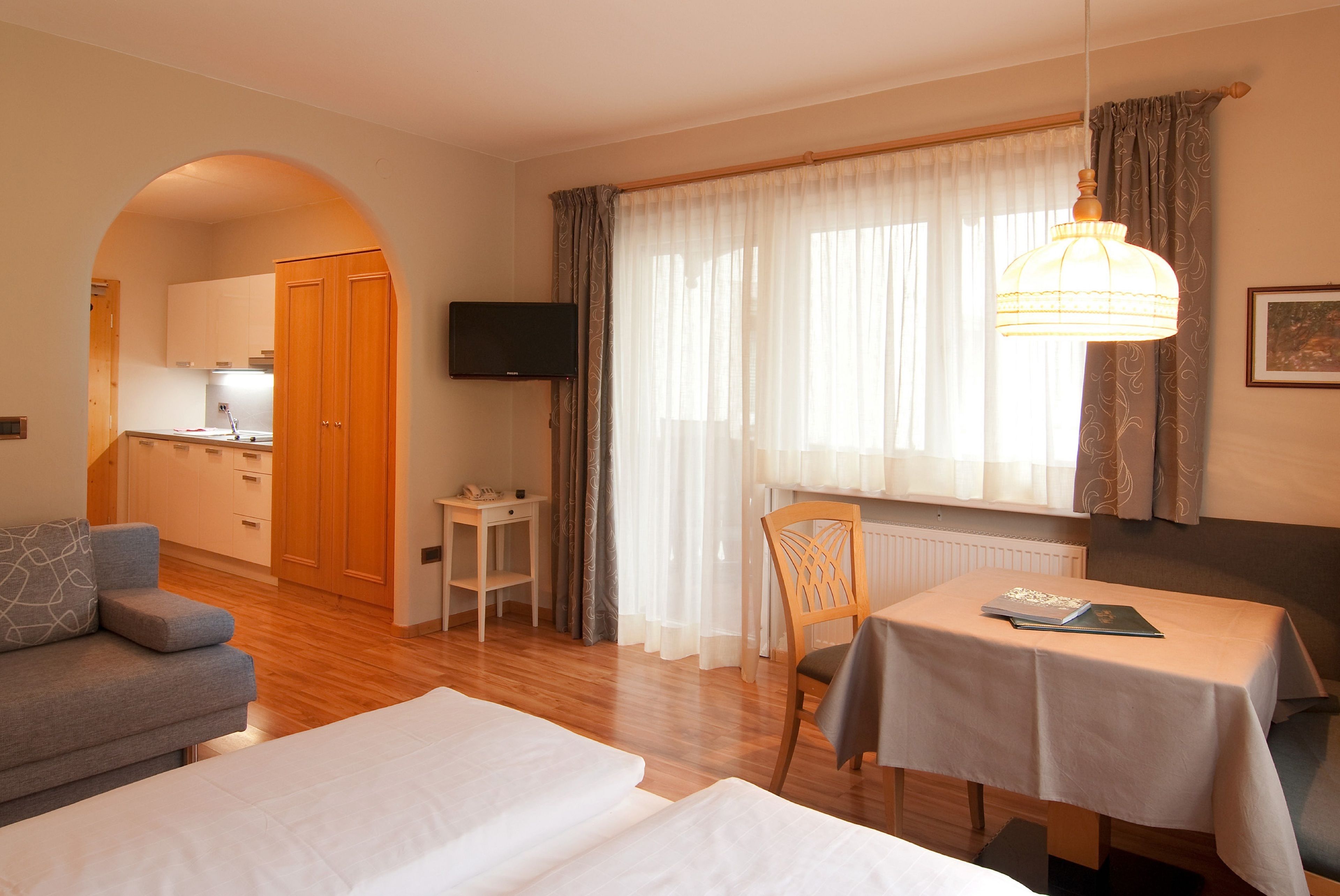 Ein Hotelzimmer mit Sofa, Bett, Esstisch, Fernseher und einer durch einen Bogen sichtbaren Küchenzeile.