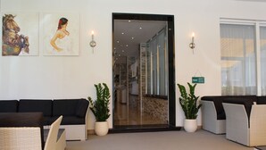 Un hall de hotel con mostrador de recepción, zona de estar y puerta de vidrio que da al pasillo.