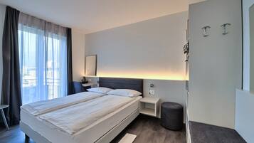 Una habitación de hotel moderna con una cama grande, mesitas de noche, un pequeño rincón de descanso y vistas al exterior.