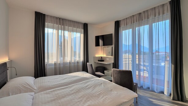 Habitación de hotel con dos camas, un escritorio, una silla, un televisor y ventanas amplias con cortinas.