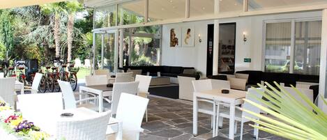 An outdoor seating area with wicker furniture, a stone floor, and a view of bicycles and greenery in the background.