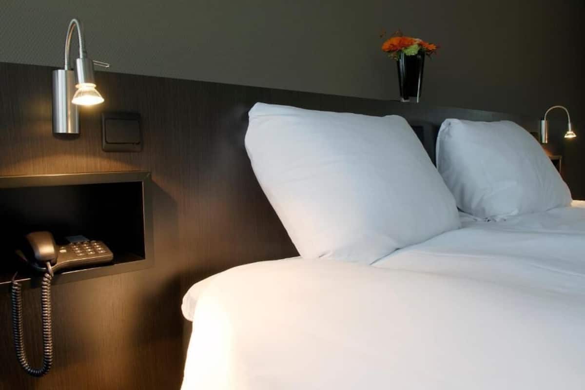 Una habitación de hotel con una cama bien hecha, un teléfono en la mesita de noche y una lámpara fijada a la pared.