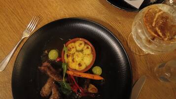 A dining table with three plates of food, a glass of beer, and a candle.
