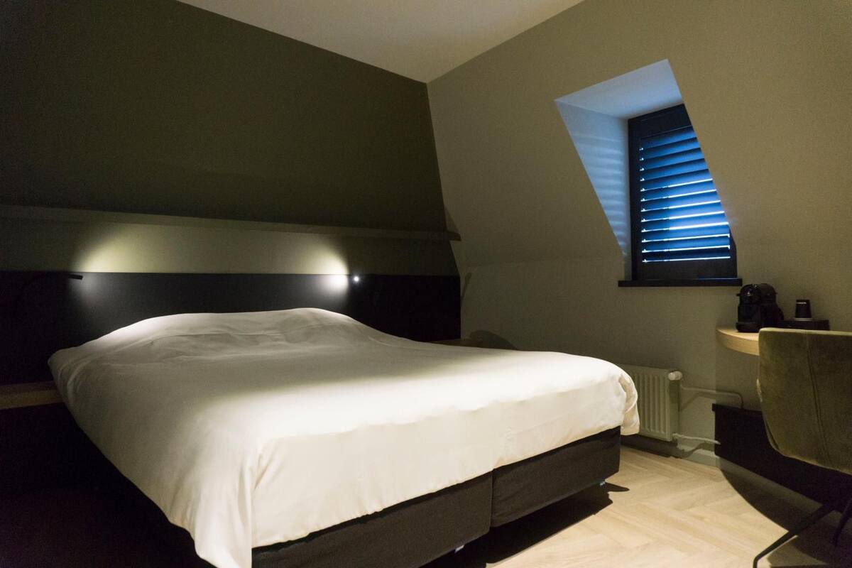 Un dormitorio con cama, una silla, un radiador y una ventana con persianas.