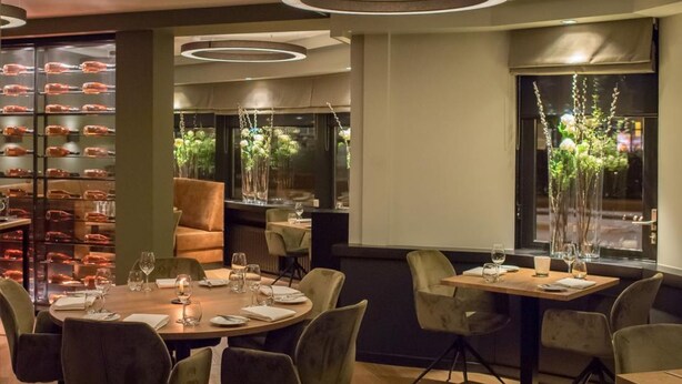 A modern dining area with round tables, chairs, and a wall displaying food items.