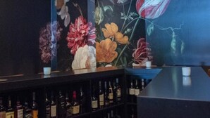 A bar area with circular ceiling lights, a floral mural, and shelves of liquor bottles.