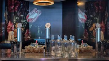 Een bar met meerdere flessen en glazen, een rieten mand met een fles, en een bloemenmuur op de achtergrond.