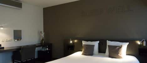 A hotel room with a large bed, a desk, and a wall with the text "SLEEP WELL".