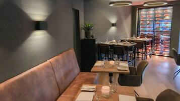 A restaurant with a modern interior, featuring a wooden table set for dining, a cushioned bench, and a display of seafood behind the counter.
