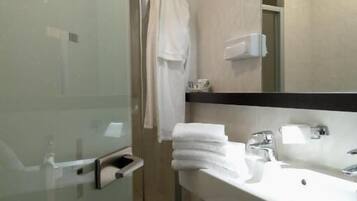 A modern bathroom with a glass shower enclosure, a white sink with a mirror above it, and a towel rack with folded towels.