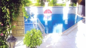 Une piscine avec un parasol rouge, entourée de verdure et d’un mur de pierre.