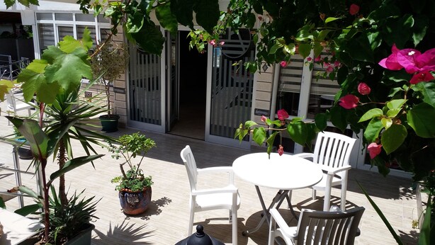 Un espace patio avec une table et des chaises blanches, entouré de plantes en pot et de plantes fleuries.
